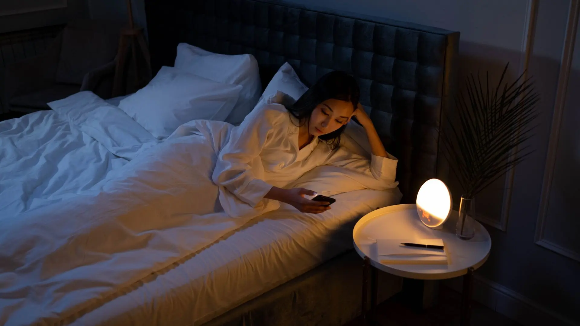 Người phụ nữ nằm trên giường bên ánh đèn ngủ vàng